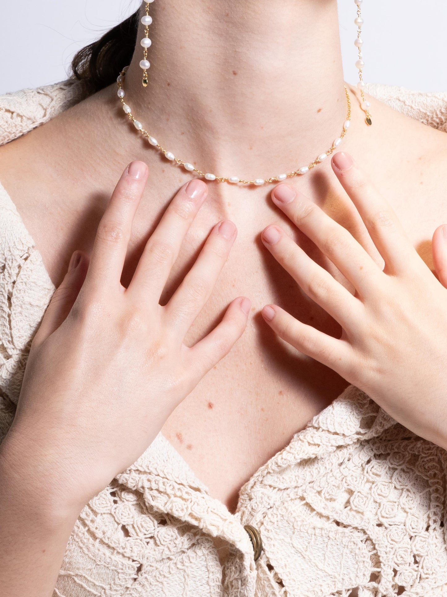 Modelo de pele branca usando colhar choker de 35 cm feito em prata com banho de ouro e com pérolas naturais de agua doce vestindo blazer de renda e brincos longos de perolas naturais com fundo branco.
