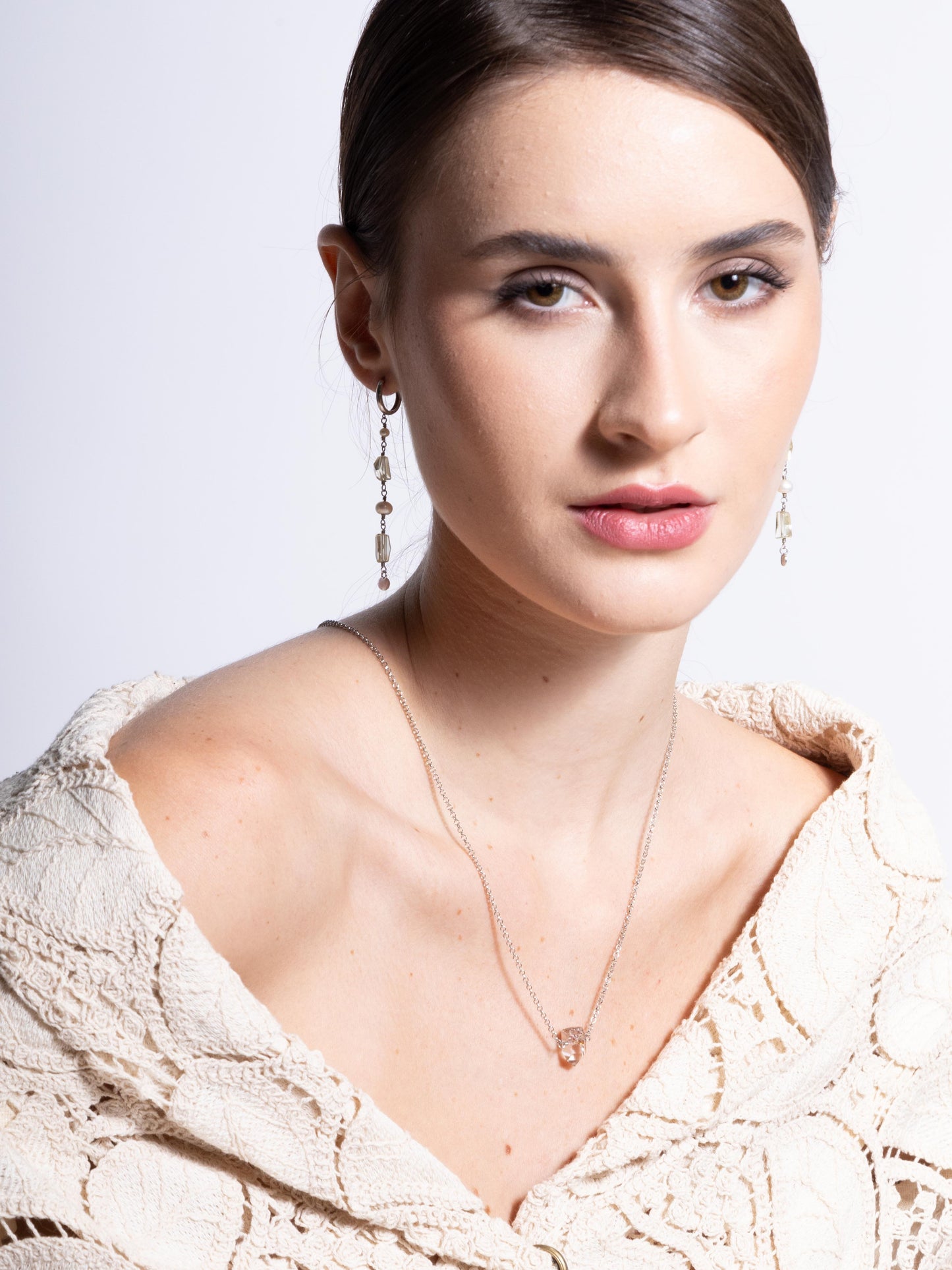 Modelo de pele branca usando Colar em corrente portuguesa de prata com uma ponta do cristal natural quartzo lodolita semi bruto com blazer de renda, brincos de perolas e cristal quartzo verde e fundo branco.