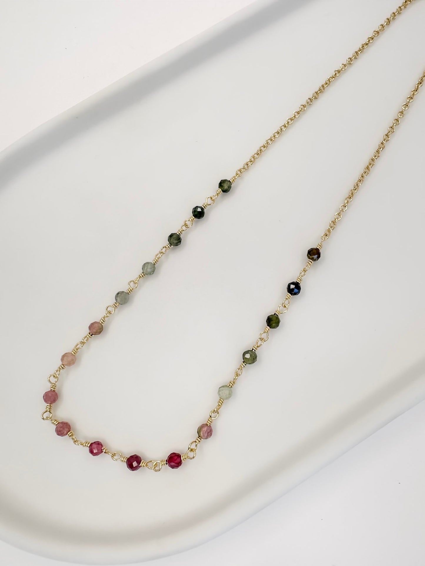 Colar tipo choker que também é Detalhe Pulseira de duas voltas de corrente portuguesa e turmaina melancia apoiada em uma bandeja branca com fundo branco.