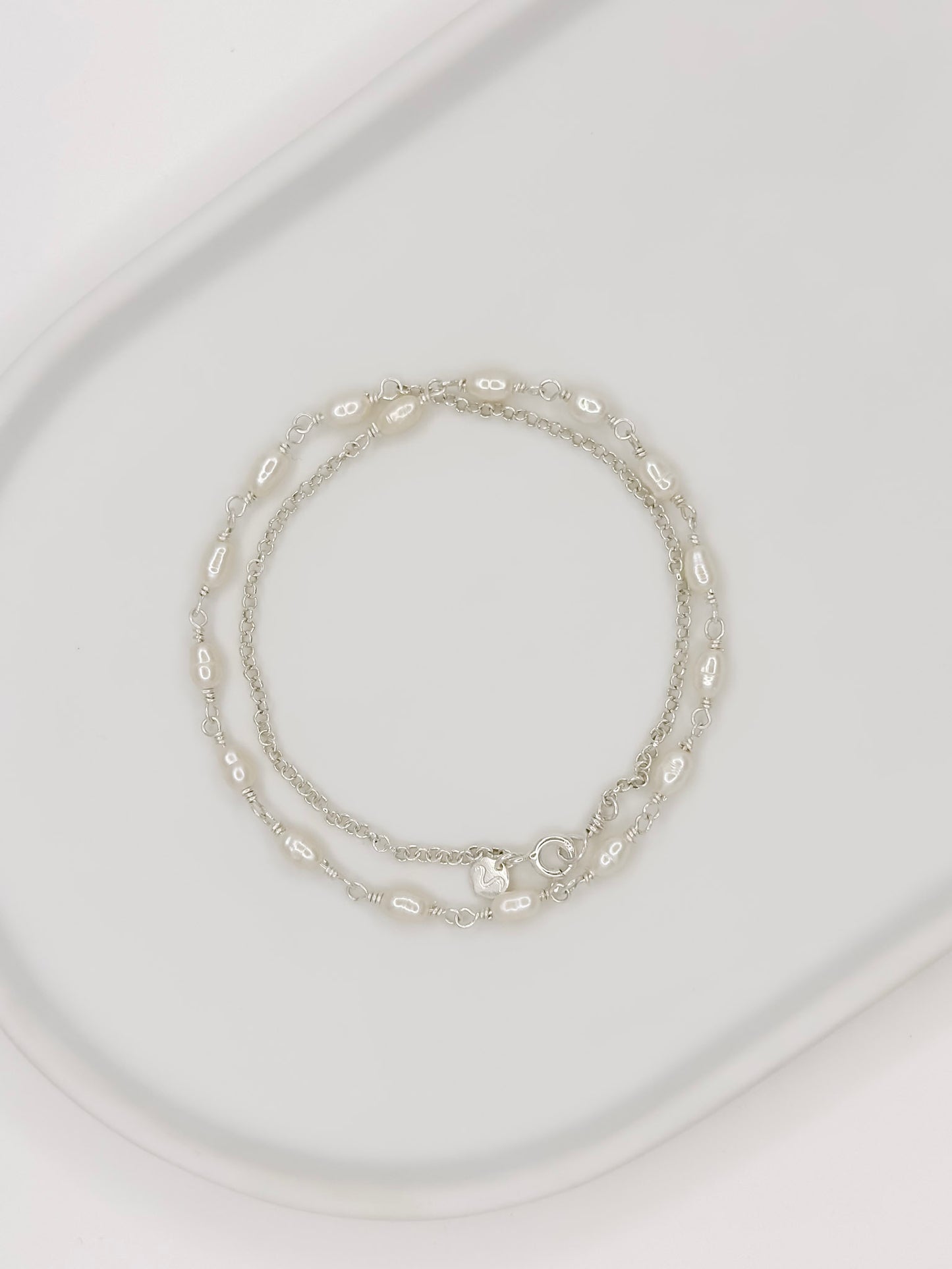 Pulseira e Colar de modelo choker feito em prata com pérolas naturais em uma bandeja branca com fundo branca com fundo branco.