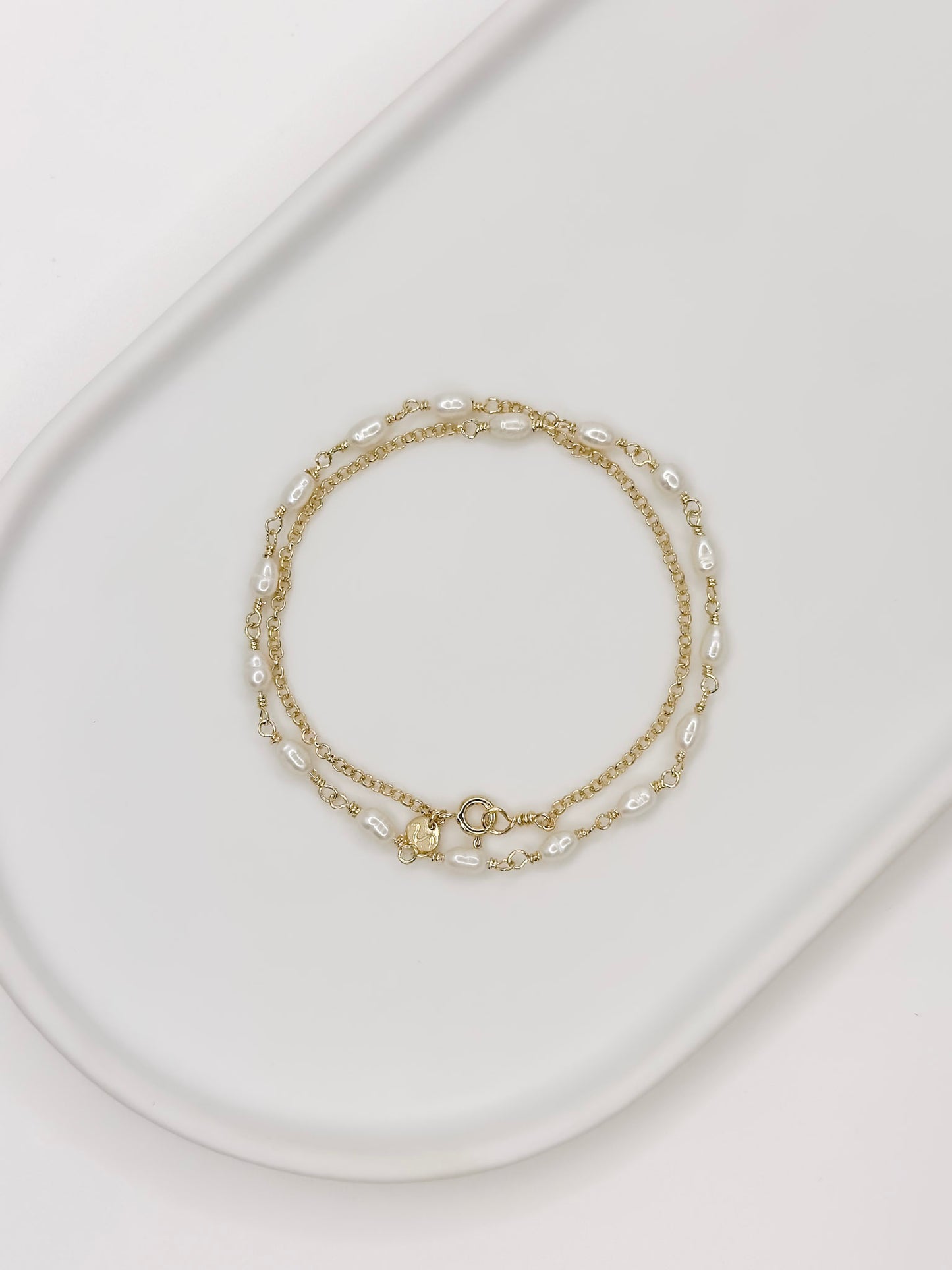 Pulseira e Colar de modelo choker feito em prata com banho de ouro e com pérolas naturais em uma bandeja branca com fundo branca com fundo branco.