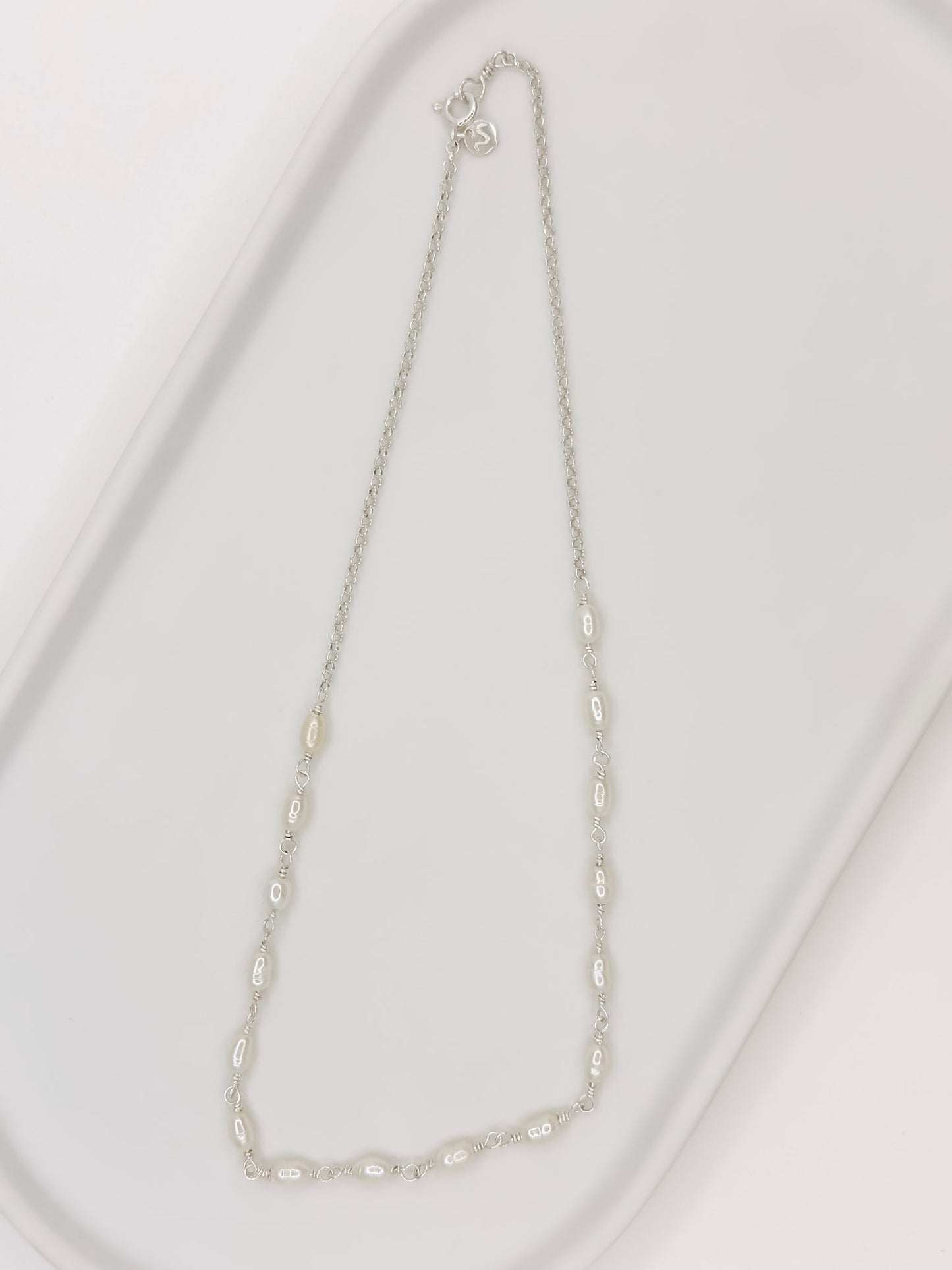 Pulseira e Colar de modelo choker feito em prata com pérolas naturais em uma bandeja branca com fundo branca com fundo branco.