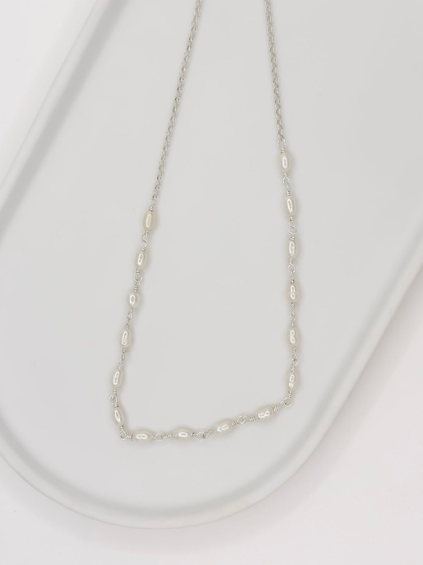 Detalhe da Pulseira e Colar de modelo choker feito em prata com pérolas naturais em uma bandeja branca com fundo branca com fundo branco.