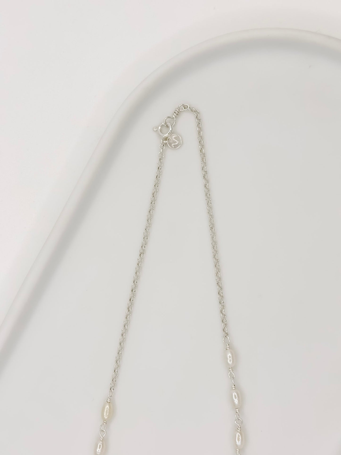 Detalhe da Pulseira e Colar de modelo choker feito com corrente portuguesa em prata e com pérolas naturais em uma bandeja branco com fundo branca com fundo branco.
