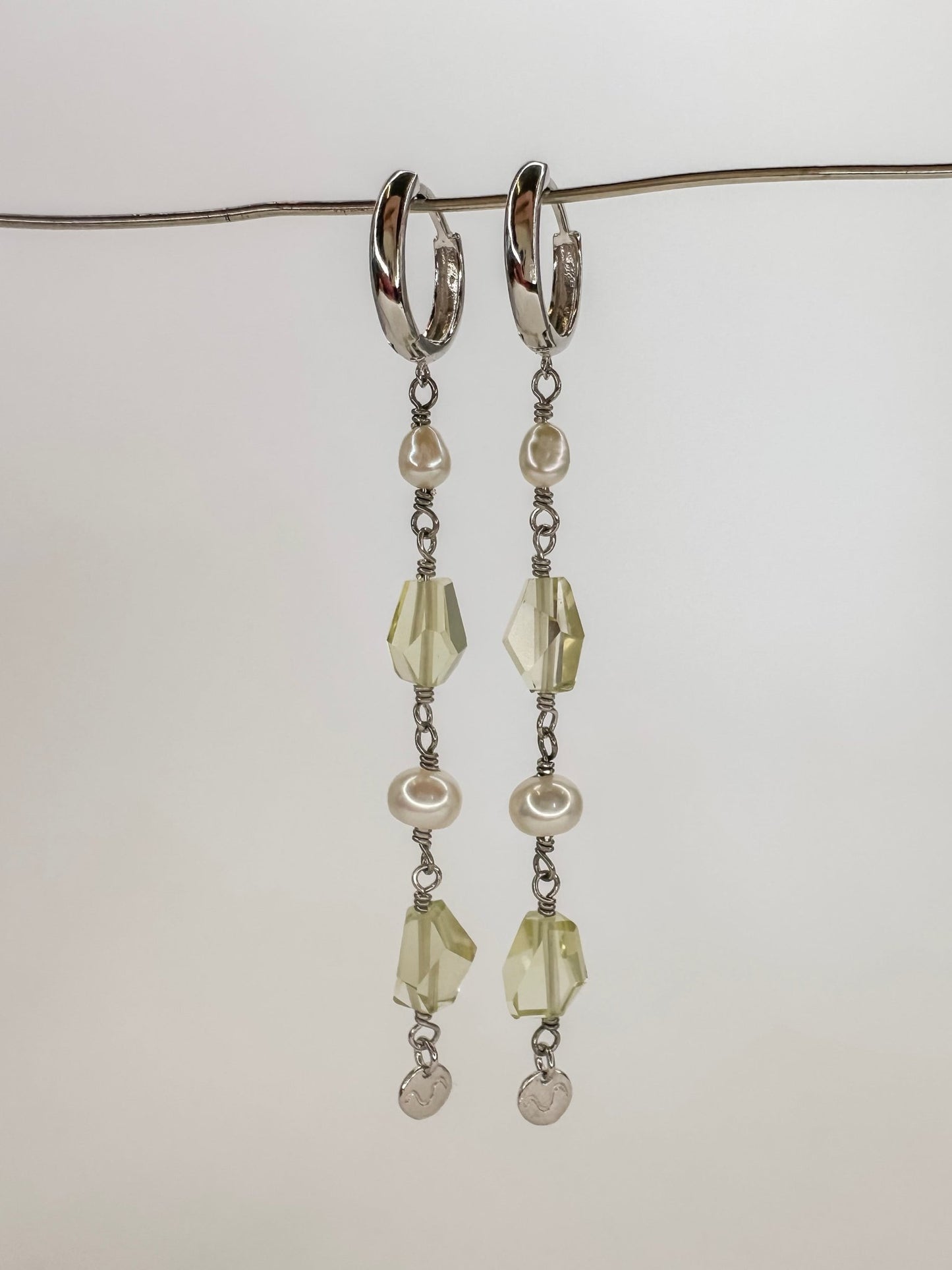 Brinco longo de argola click em prata com banho de ouro branco com duas pedras de quartzo limao ou quartzo verde lapidadas e duas perolas tendo o cumprimento longo e com uma plaquinha pendurada no final, com fundo branco.