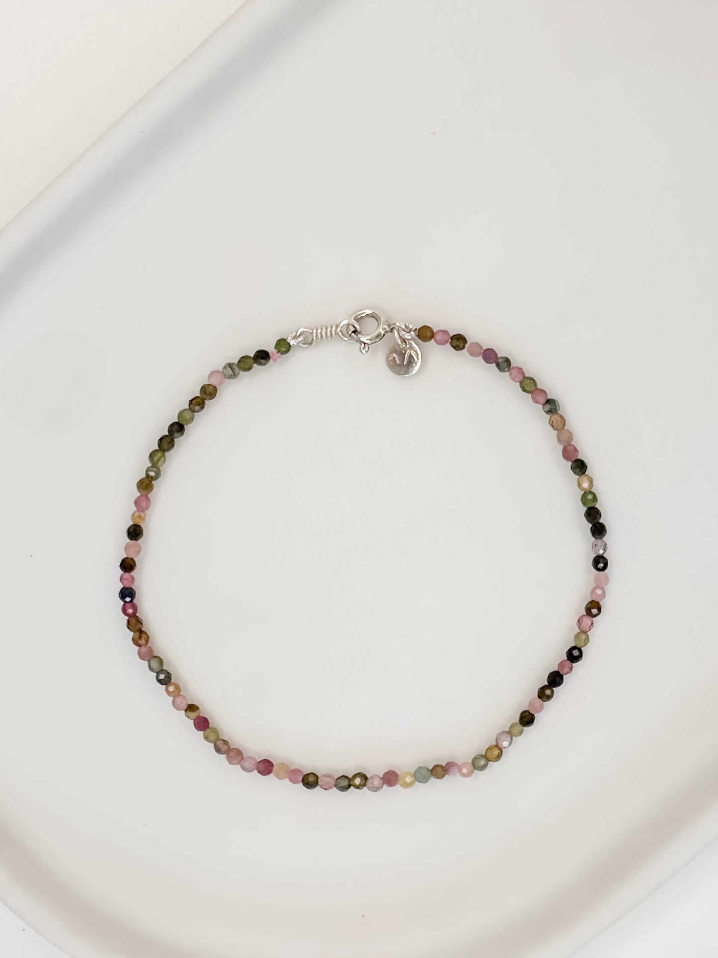 Pulseira com cristais naturais de turmalinas coloridas com fecho boia em prata apoiada em uma ceramica branca e fundo branco.