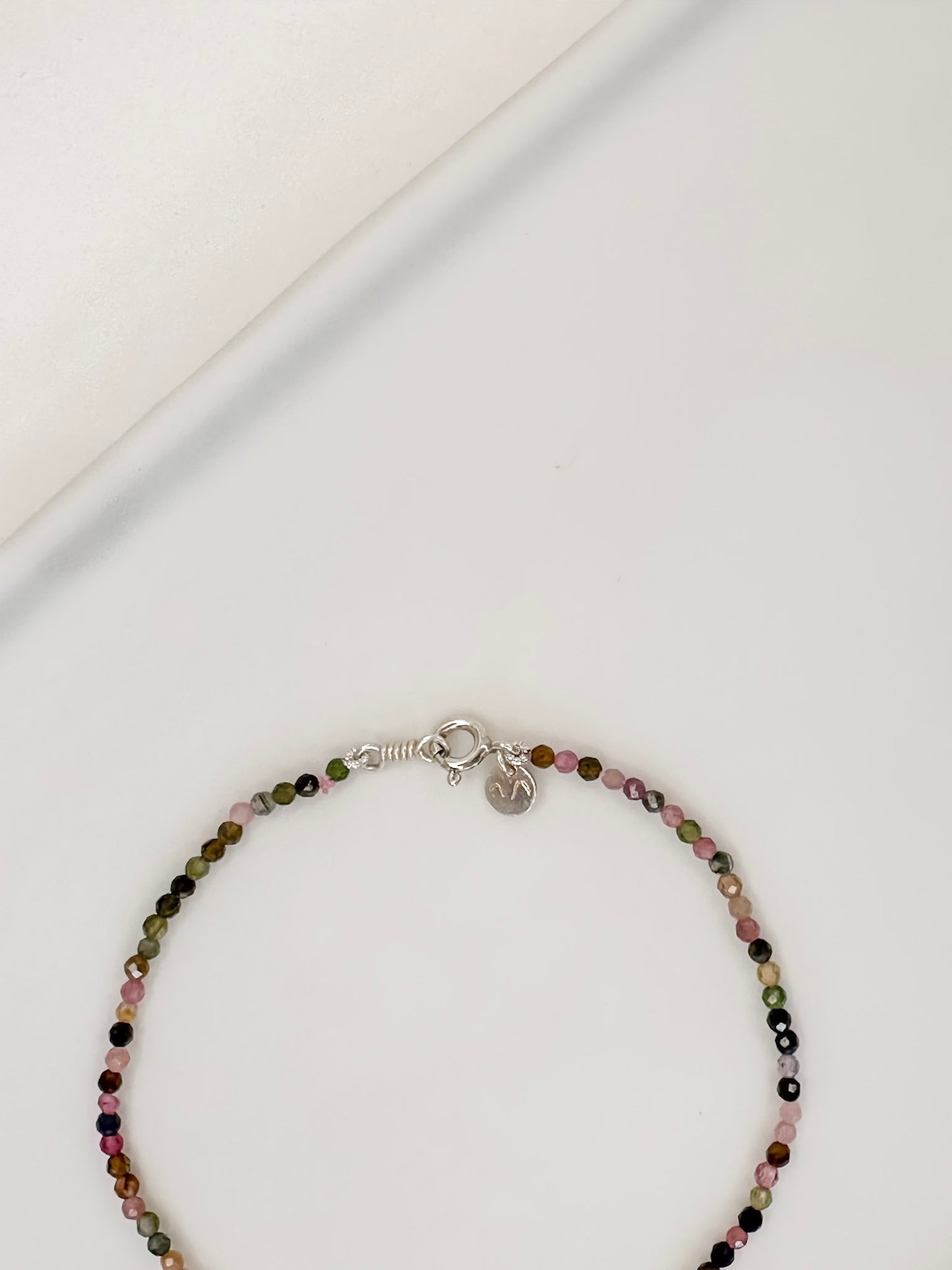 Pulseira com cristais naturais de turmalinas coloridas com fecho boia em prata apoiada em uma ceramica branca e fundo branco.