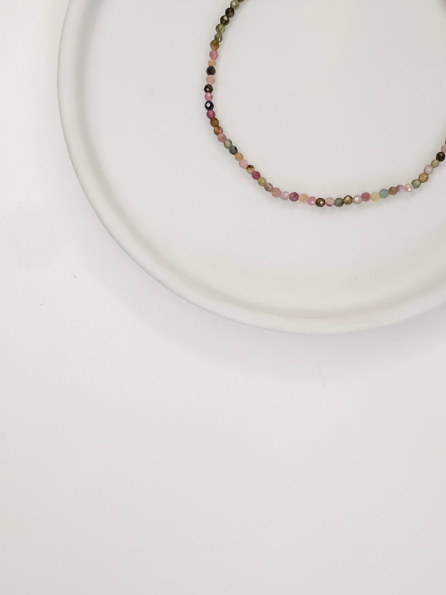 Pulseira com cristais naturais de turmalinas coloridas apoiada em uma ceramica branca e fundo branco.