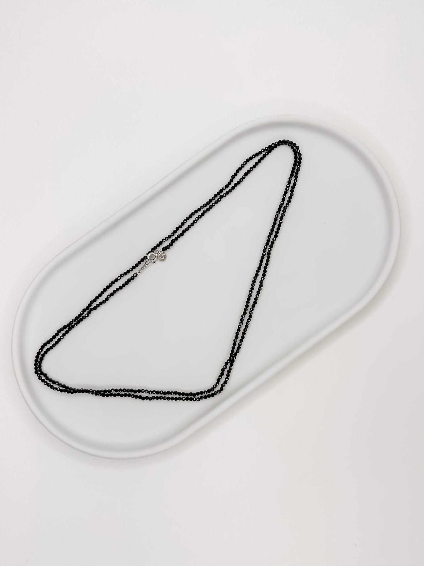 Colar produzido com esferas facetadas de espinelio natural medindo aproximadamente 2mm cada, com fecho em prata 925, apoiado em bandeja de ceramica branca com fundo branco.