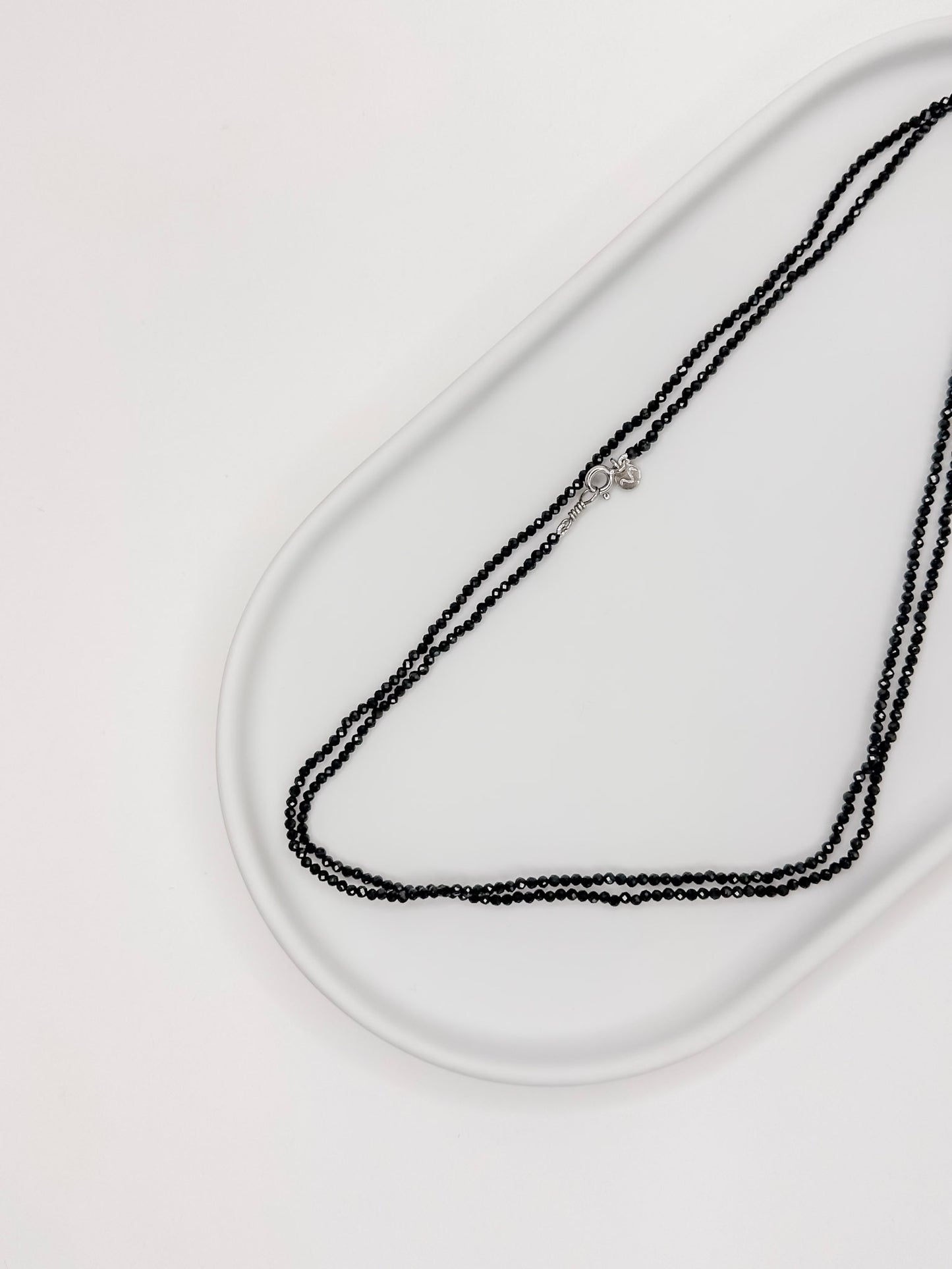 Colar produzido com esferas facetadas de espinelio natural medindo aproximadamente 2mm cada, com fecho em prata 925, apoiado em bandeja de ceramica branca com fundo branco.