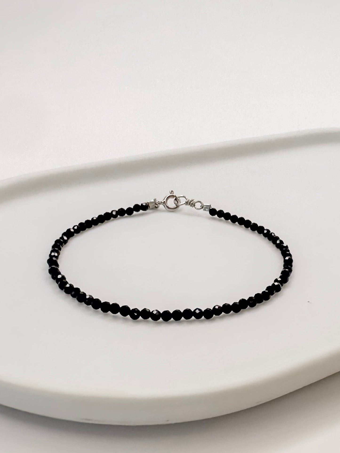 Pulseira produzida com esferas facetadas de espinelio natural medindo aproximadamente 2mm cada, com fecho em prata 925, apoiado em bandeja de ceramica branca e fundo branco.