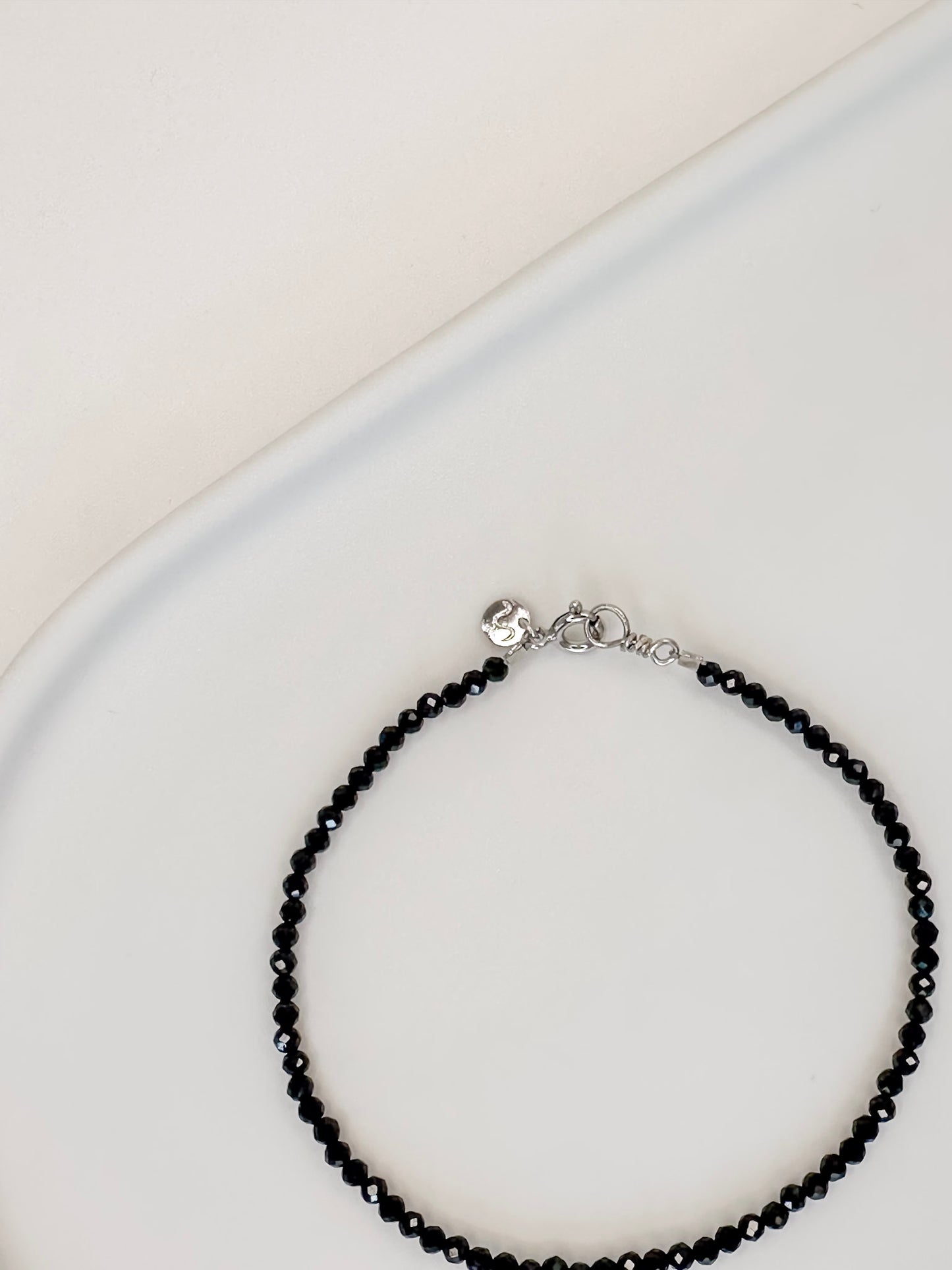 Pulseira produzida com esferas facetadas de espinelio natural medindo aproximadamente 2mm cada, com fecho em prata 925, apoiado em bandeja de ceramica branca e fundo branco.