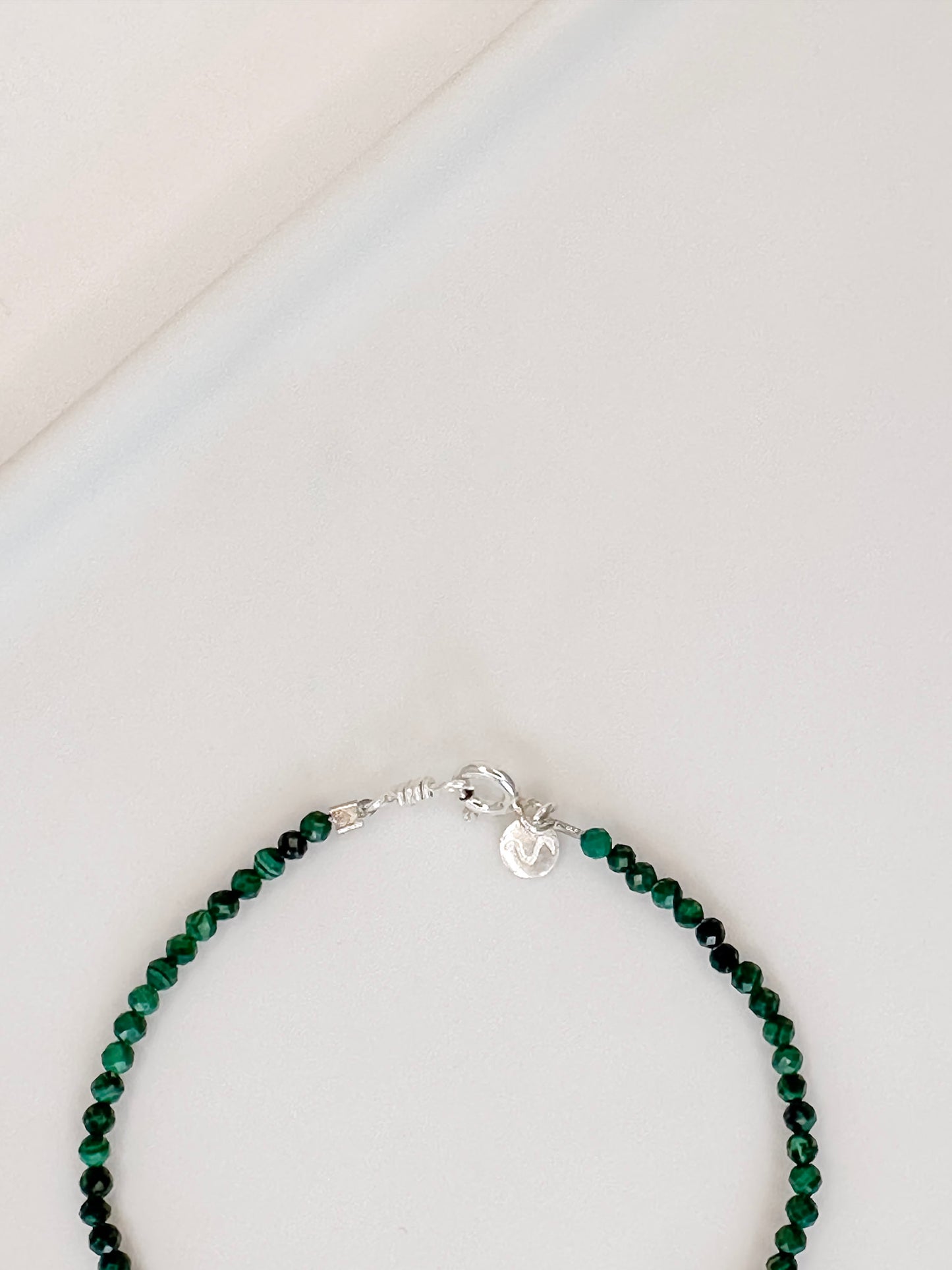 Pulseira com pedra malaquita natural com esferas lapidadas de aproximadamente 2mm apoiada em bandeja de ceramica branca com fundo branco.