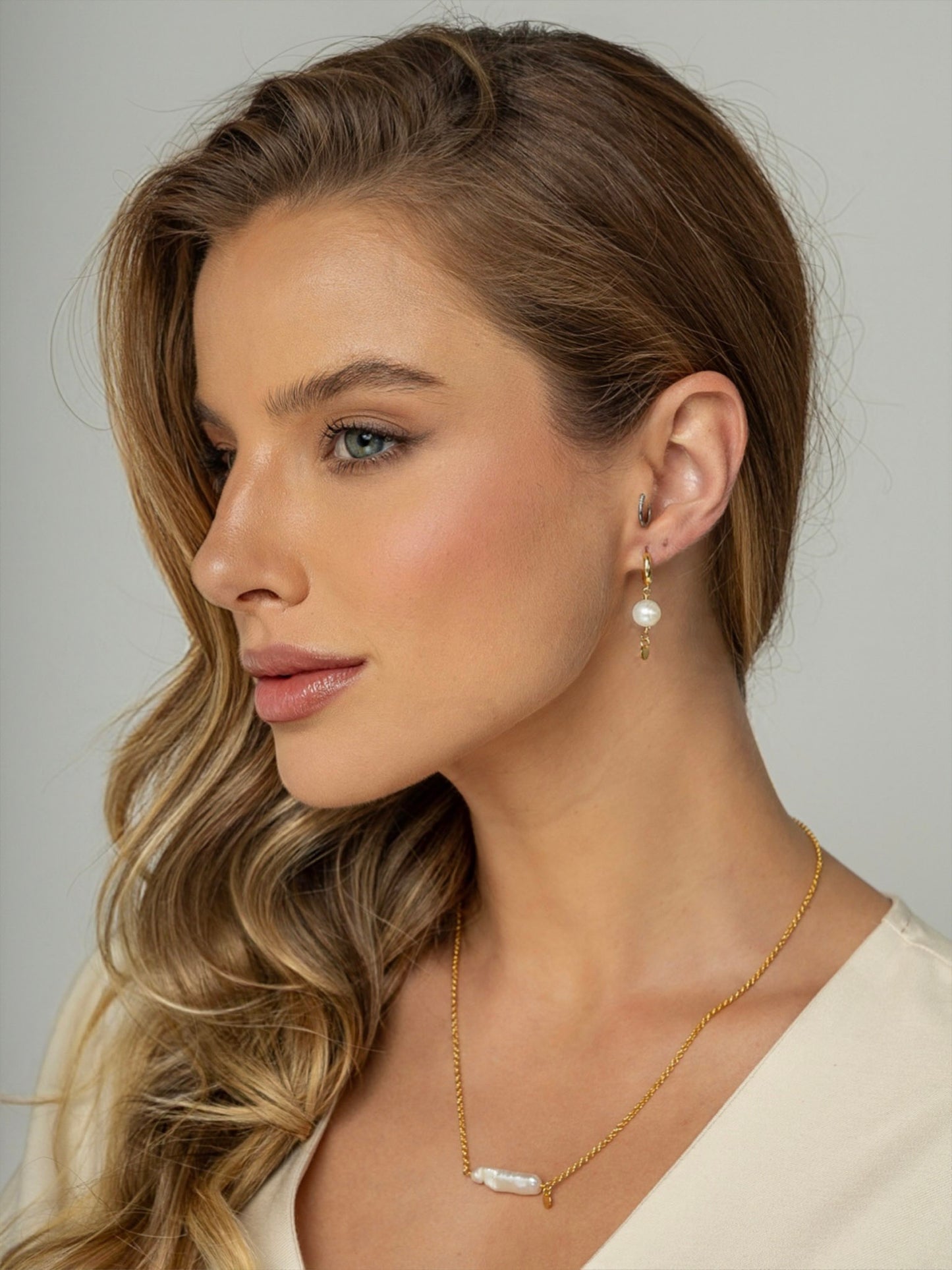 Modelo veste colar com corrente portuguesa em prata 925 e banho de ouro 18k com uma perola barroca natural fixa no formato palito no centro.