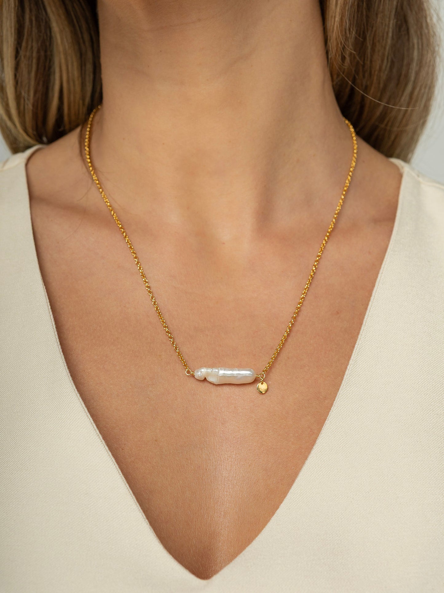 Modelo veste colar com corrente portuguesa em prata 925 e banho de ouro 18k com uma perola barroca natural fixa no formato palito no centro.