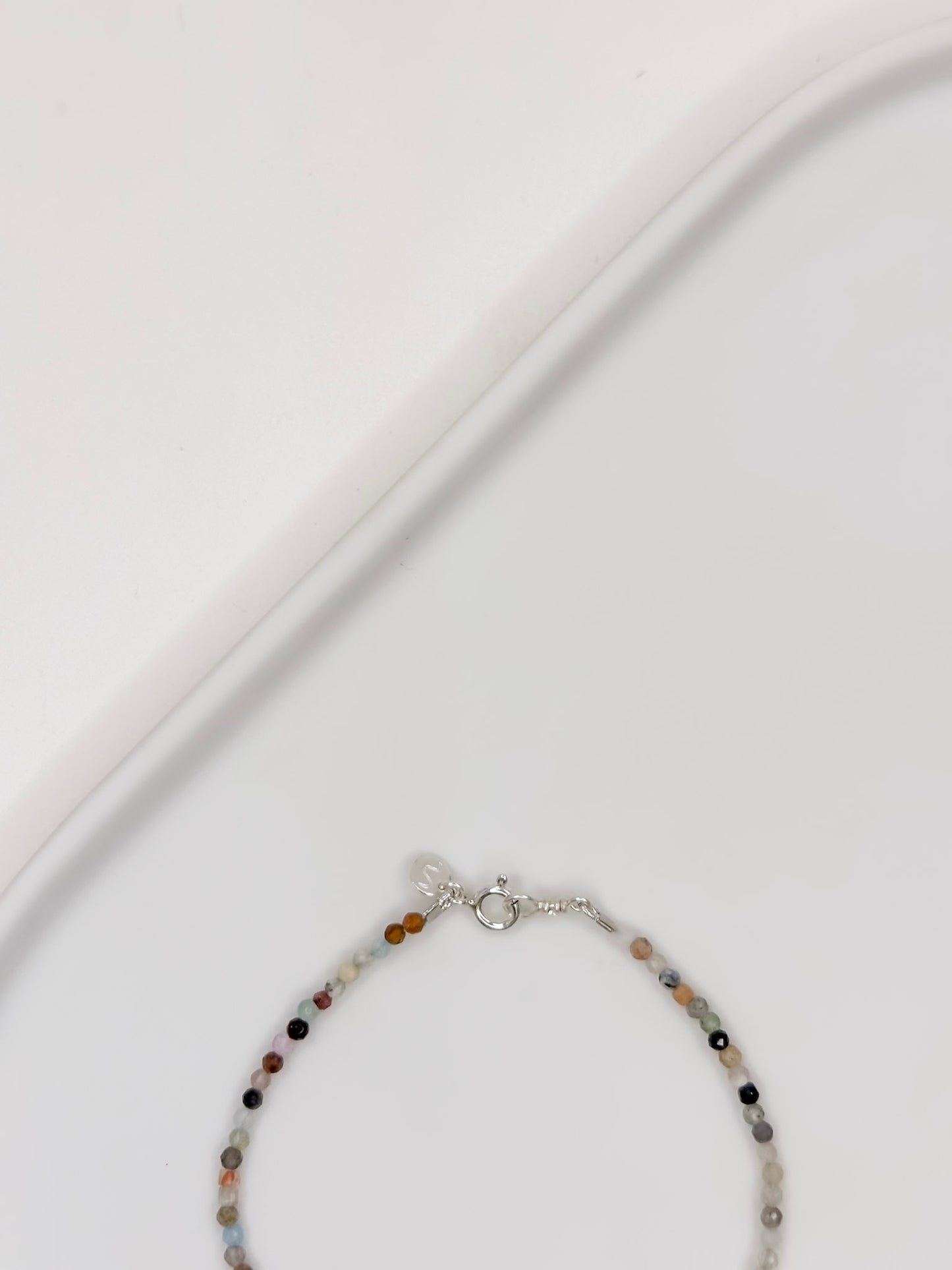 Pulseira com mix de cristais em esferas facetadas de 2 mm cada com fecho boia em prata apoiada em bandeja de ceramica branca.