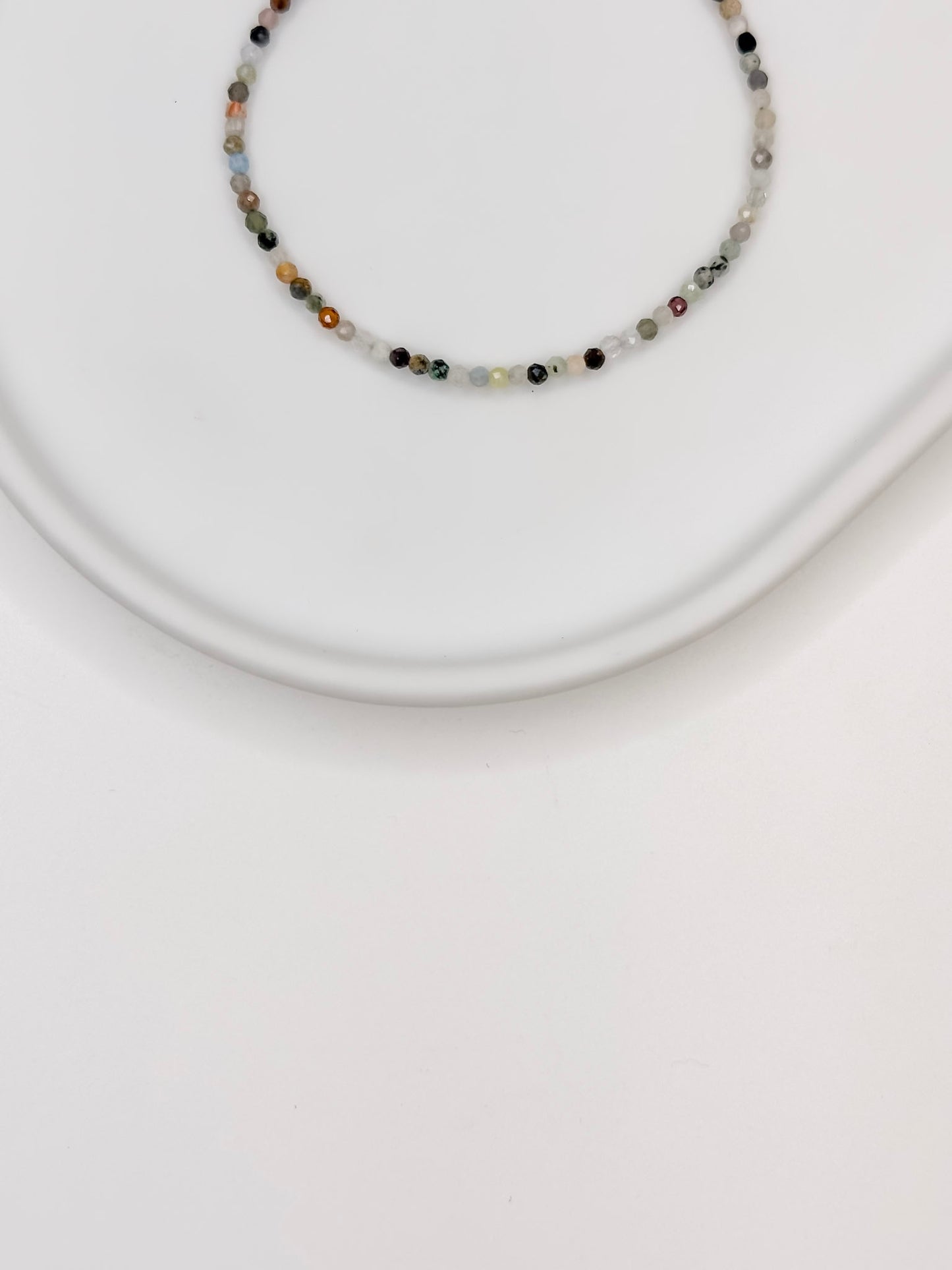 Pulseira com mix de cristais em esferas facetadas de 2 mm cada com fecho boia em prata apoiada em bandeja de ceramica branca.