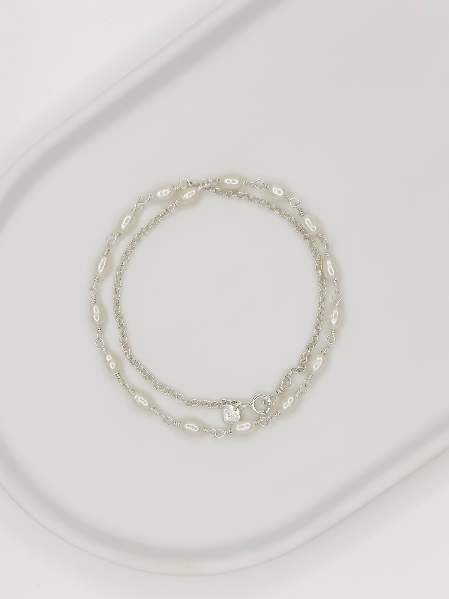 Pulseira e Colar de modelo choker feito em prata com pérolas naturais em uma bandeja branca com fundo branca com fundo branco. 