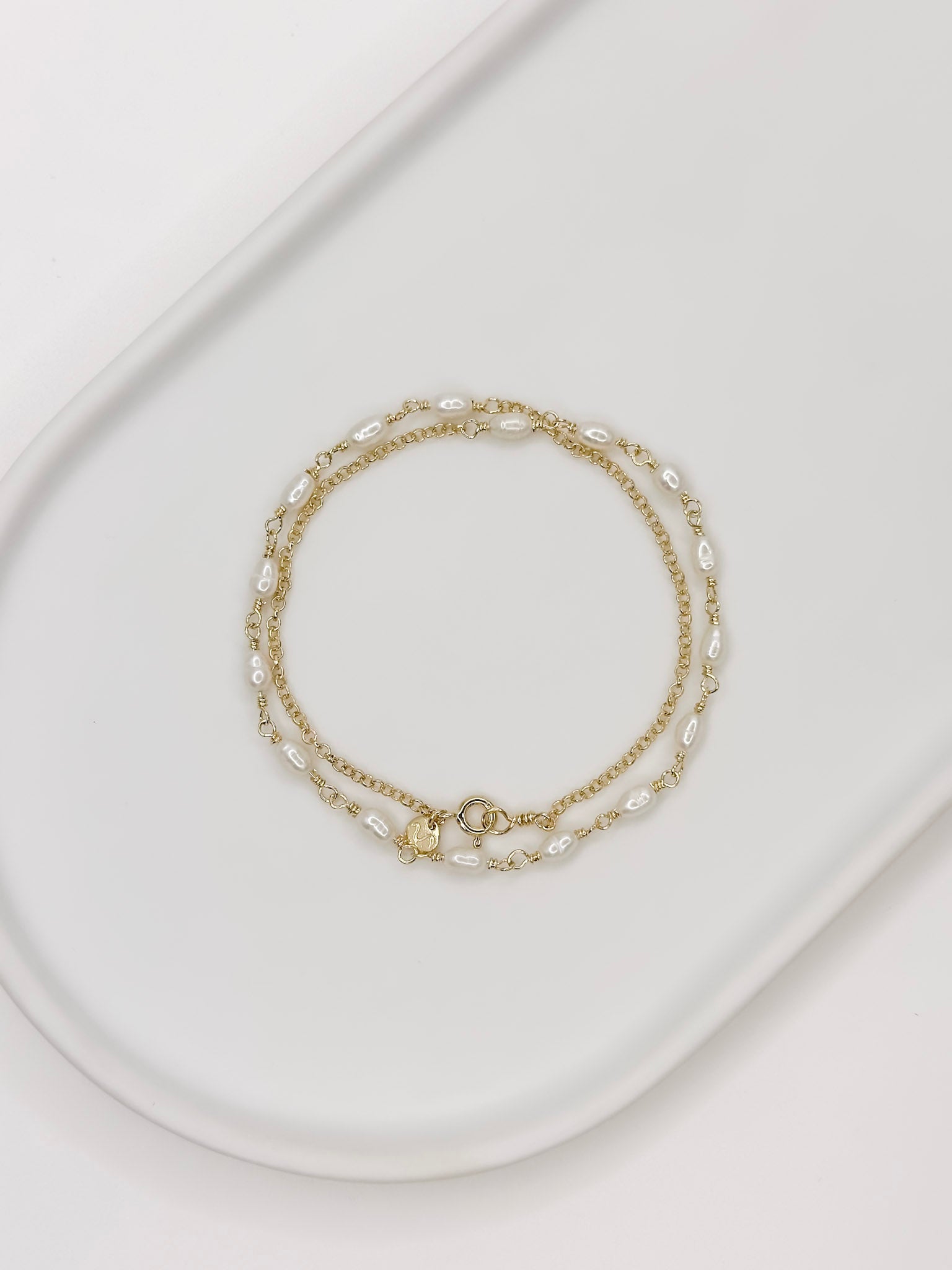 Pulseira e Colar de modelo choker feito em prata com banho de ouro e com pérolas naturais em uma bandeja branca com fundo branca com fundo branco. 