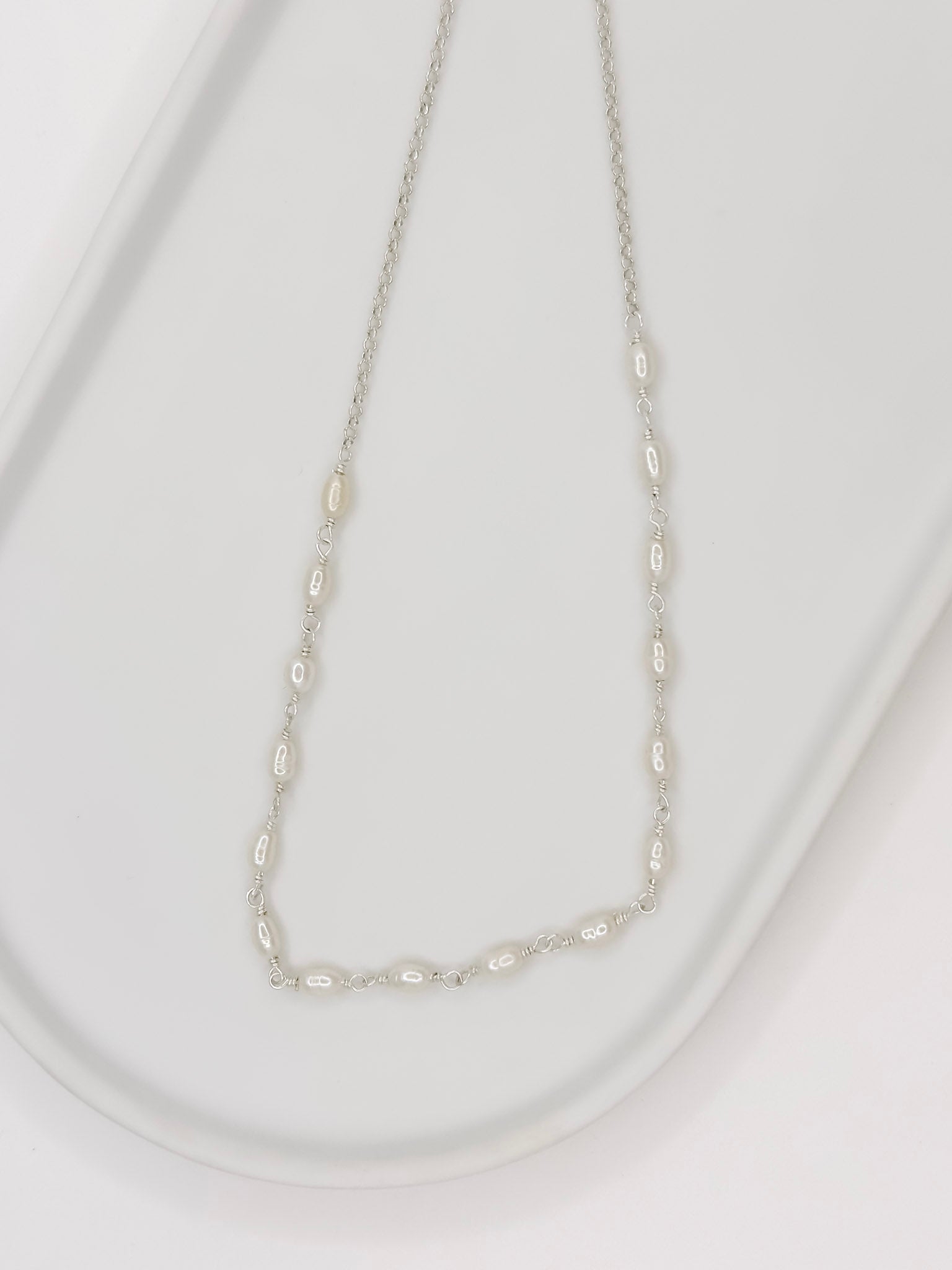 Detalhe da Pulseira e Colar de modelo choker feito em prata com pérolas naturais em uma bandeja branca com fundo branca com fundo branco. 