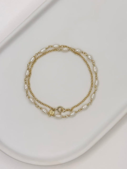 Pulseira e Colar de modelo choker feito em prata com pérolas naturais em uma bandeja brancoenrolado em um cilindro com fundo branca com fundo branco. 