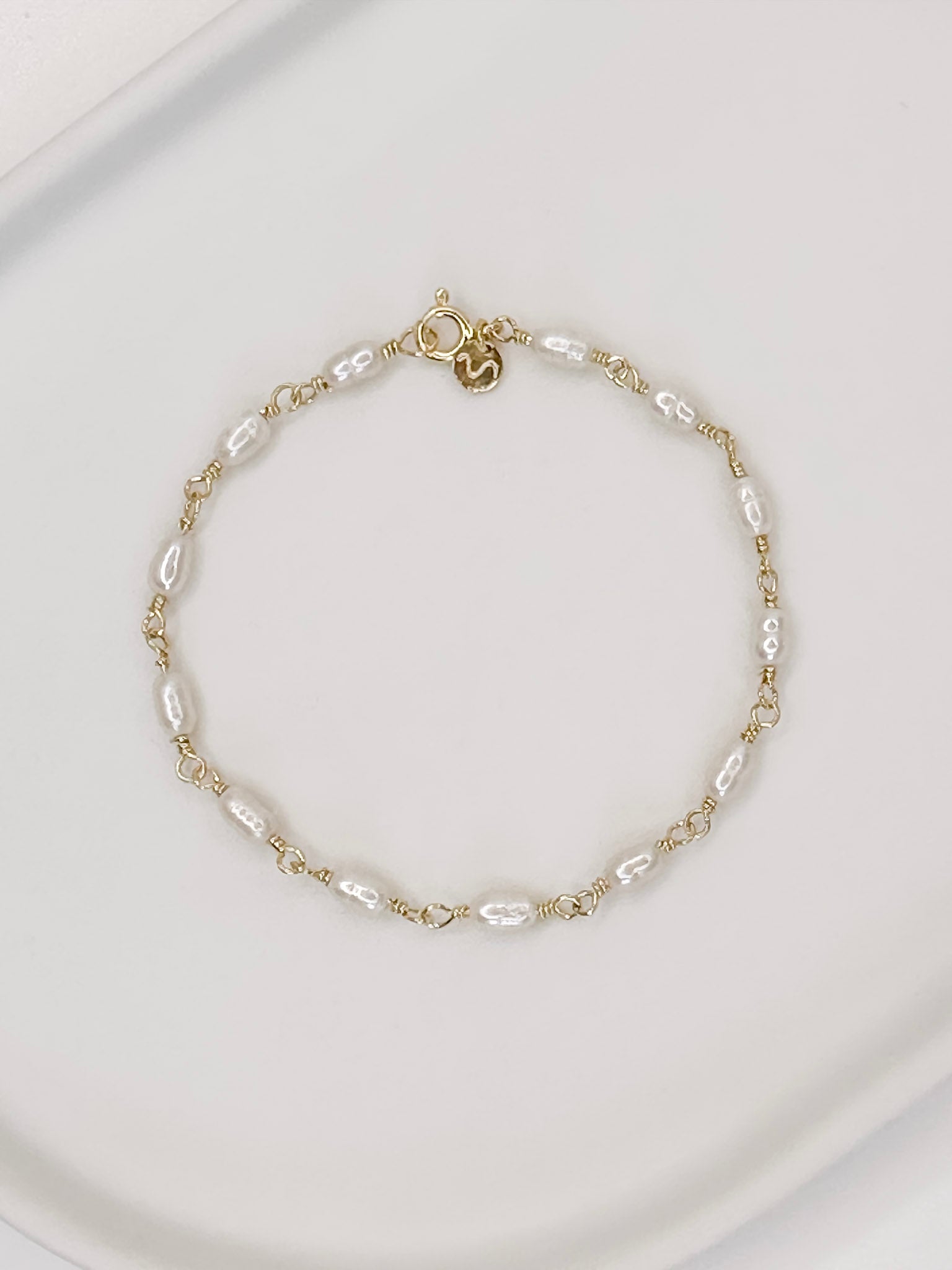 Pulseira feita a mão em prata 925 com banho de ouro e pérolas naturais de água doce, apoiada em uma bandeja de ceramica branca com fundo branco.