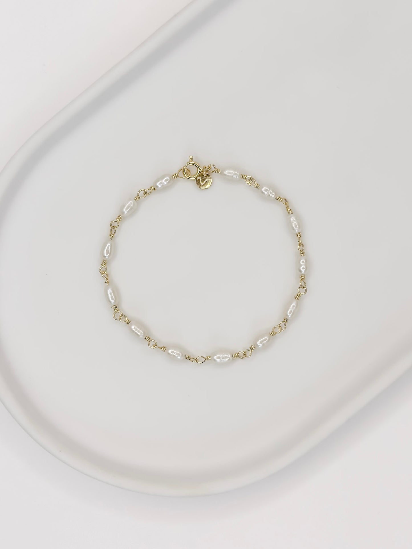 Pulseira feita a mão em prata 925 com banho de ouro e pérolas naturais de água doce, apoiada em uma bandeja de ceramica branca com fundo branco.