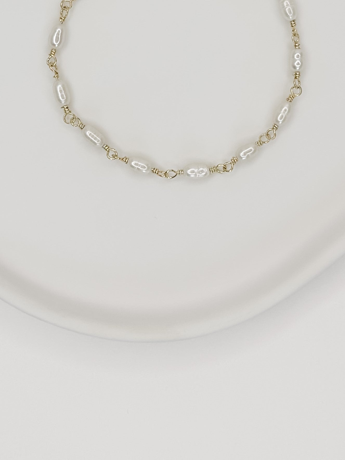 Pulseira feita a mão em prata 925 com banho de ouro e pérolas naturais de água doce, apoiada em uma bandeja de ceramica branca com fundo branco.