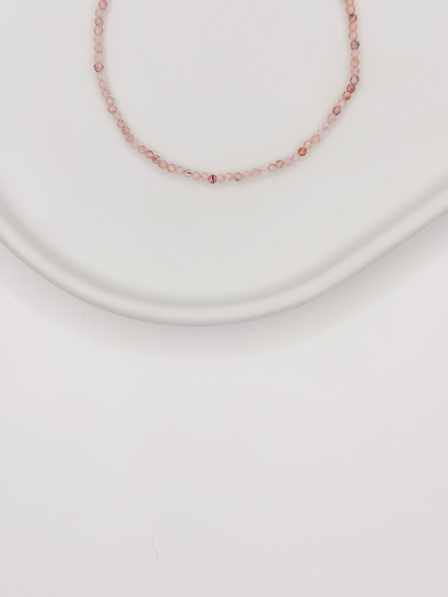 Pulseira produzida com esferas lapidadas de quartzo rosa natural de aproximadamente 2mm com fecho boia em prata apoiada em bandeja de ceramica branca com fundo branco.