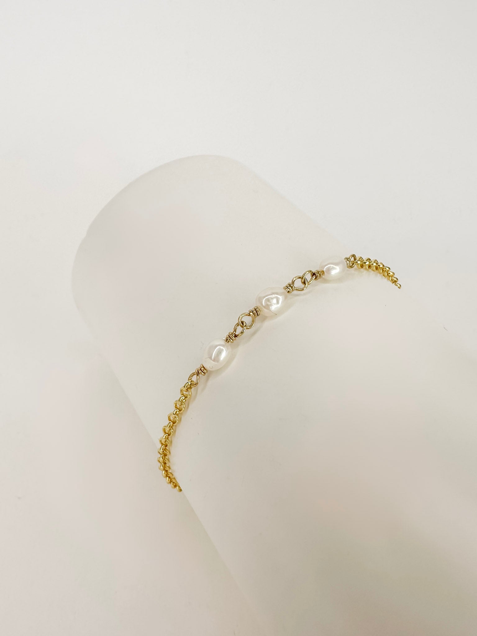 Pulseira feita com corrente portuguesa em prata 925 com banho de ouro 18K e 3 pérolas naturais em cilindro branco com fundo branco.