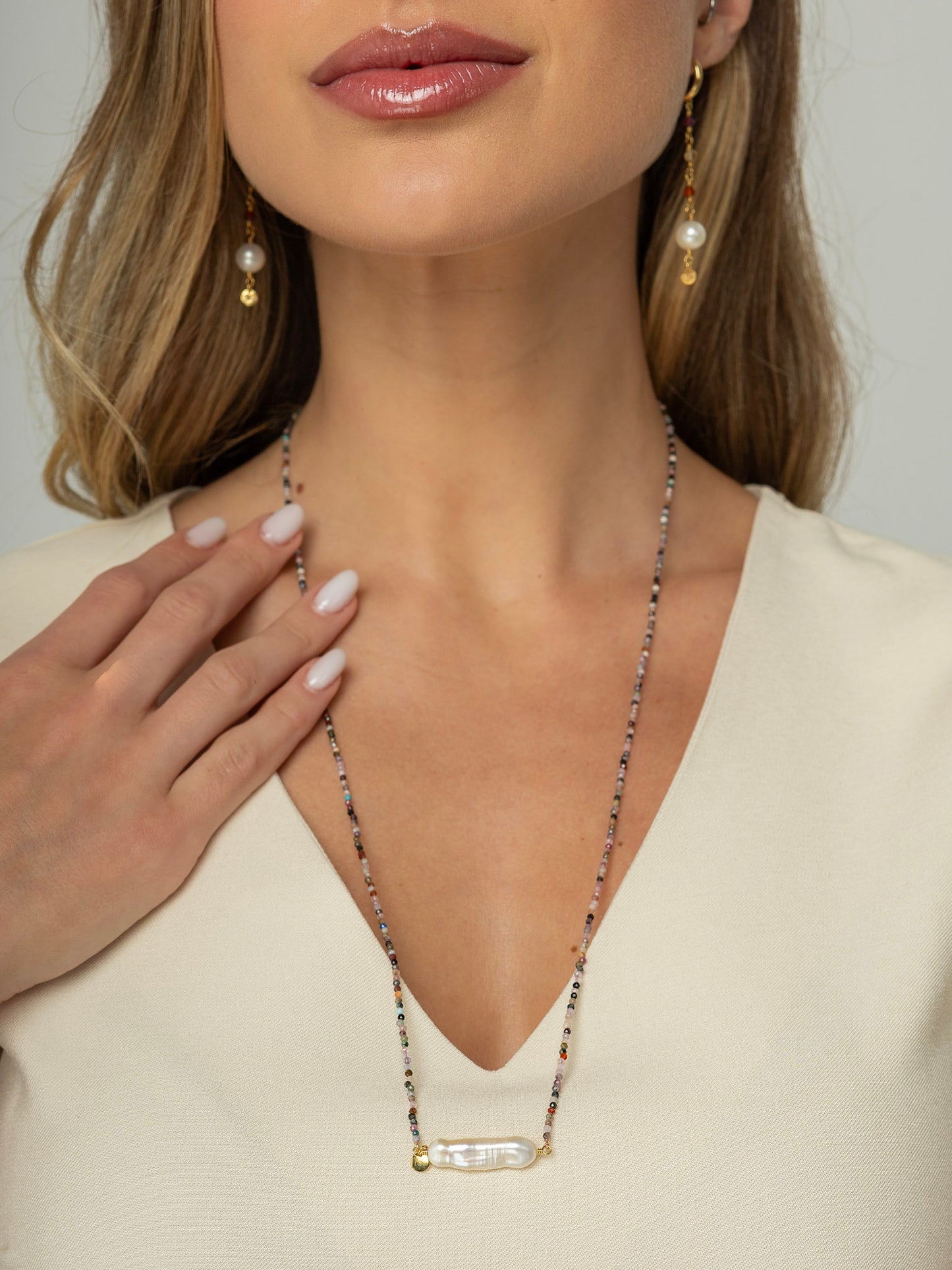 Modelo veste colar com fio em pedras e cristais naturais de aproximadamente 2mm cada com cumprimento de 70cm e uma perola barroca palito no centro fixada com fio em prata 925 e uma plaquinha redonda da marca. 