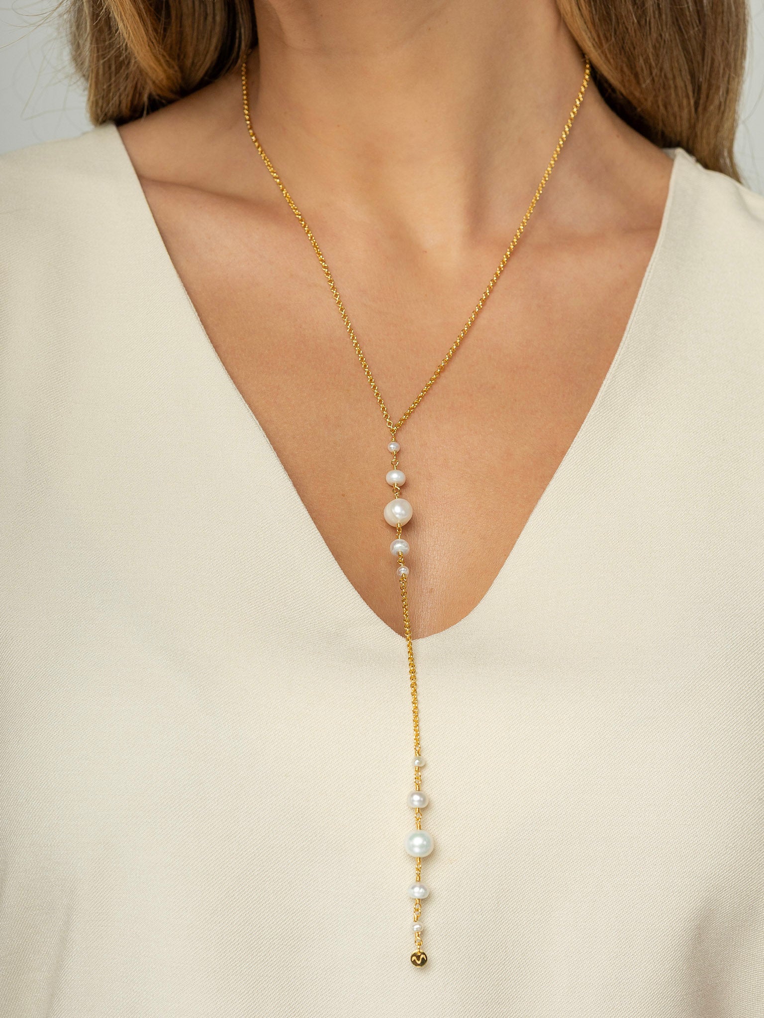 Modelo veste colar em formato Y com corrente portuguesa e pérolas redondas naturais em diferentes tamanhos, feito em prata 925 com banho de ouro. 
