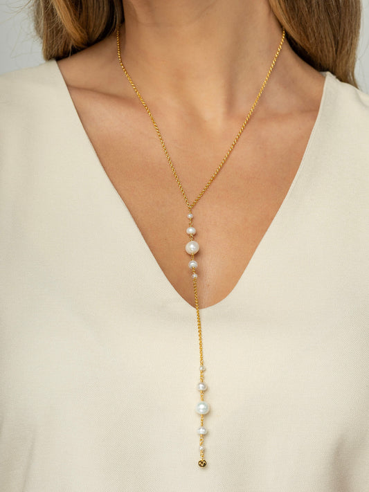 Modelo veste colar em formato Y com corrente portuguesa e pérolas redondas naturais em diferentes tamanhos, feito em prata 925 com banho de ouro. 