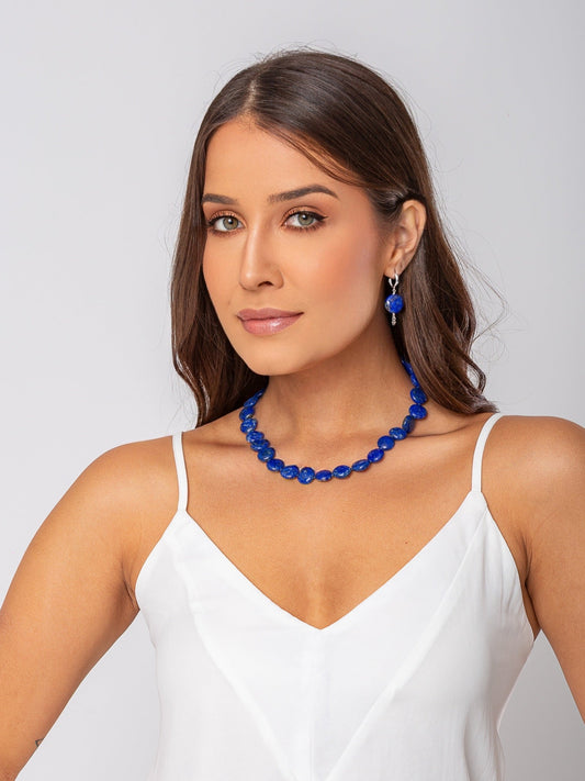 Modelo veste colar produzido com Lápis Lázuli natural em formato de moedas medindo aproximadamente 15mm cada com fecho em prata 925, e brinco em argola click de prata 925 com uma pedra lápis lázuli natural de 15mm.