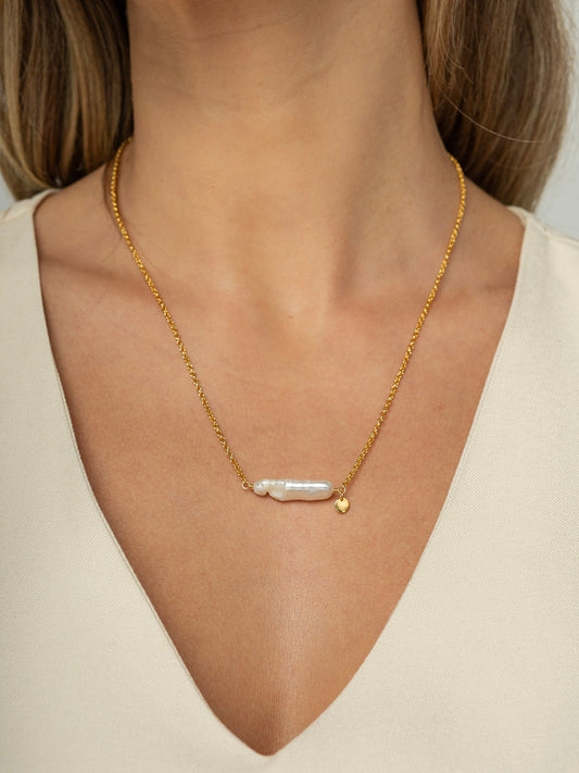 Modelo veste colar com corrente portuguesa em prata 925 e banho de ouro 18k com uma perola barroca natural fixa no formato palito no centro.